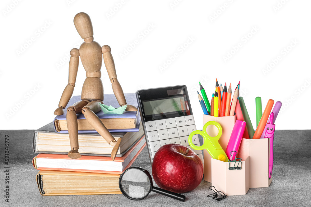 Cups with school stationery, mannequin and apple on table against white background