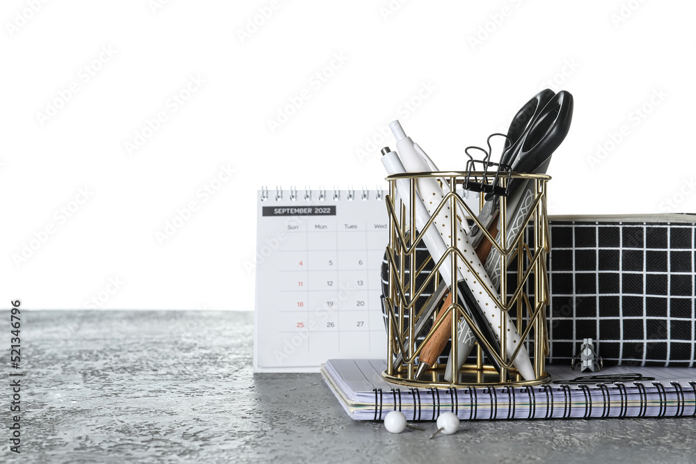 Cup with school stationery, pencil case and calendar on table against white background