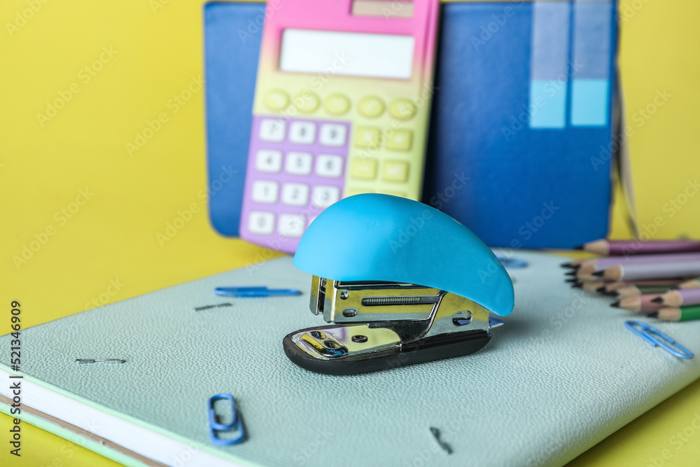 Stapler with stationery supplies on yellow background, closeup