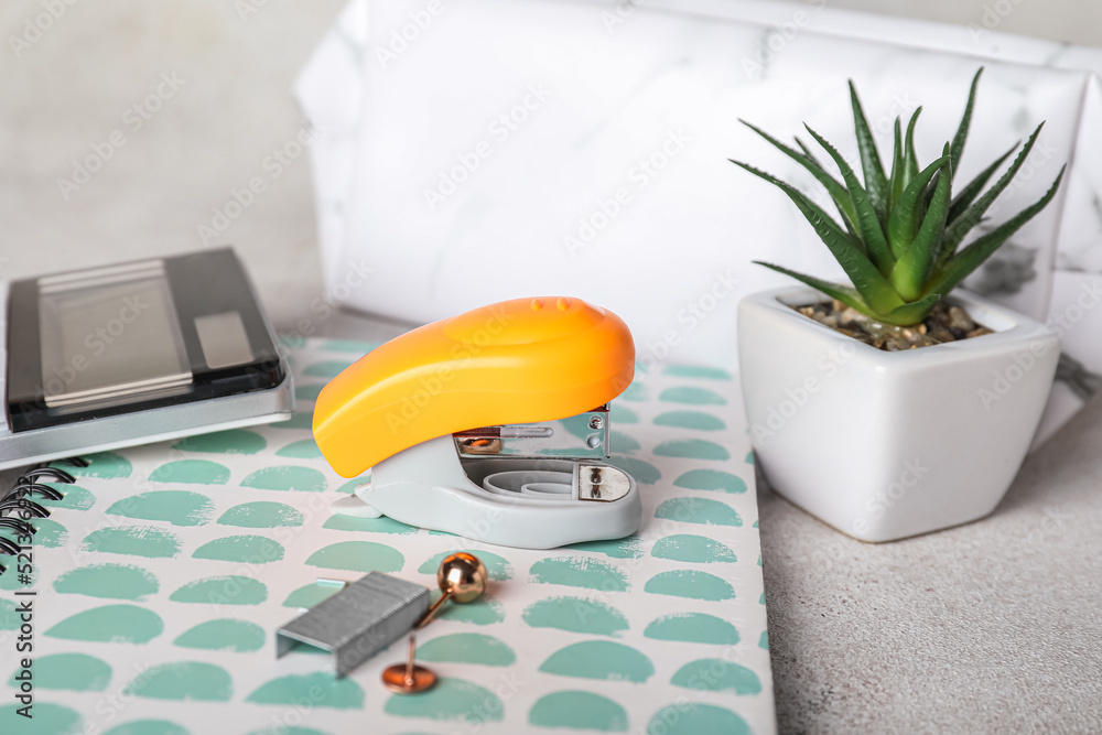 Stapler with stationery supplies and flowerpot on light background, closeup