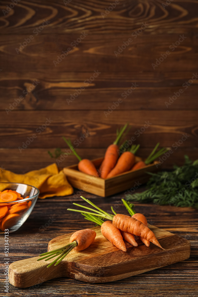 Board with fresh carrots on wooden background