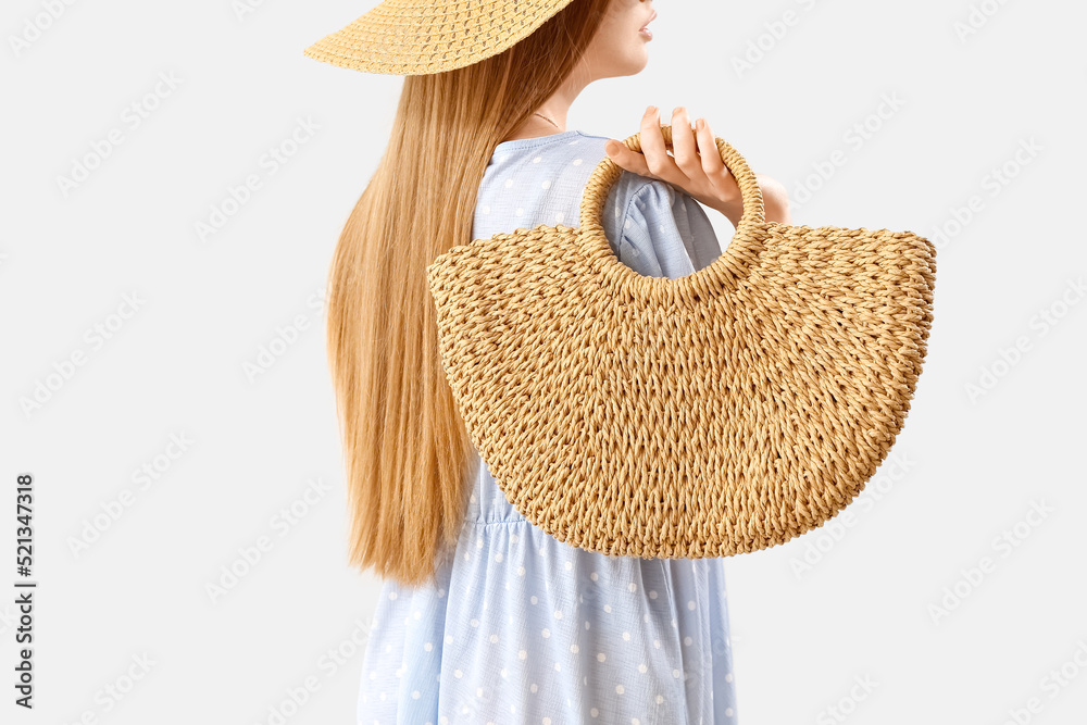 Young woman holding rattan handbag on light background