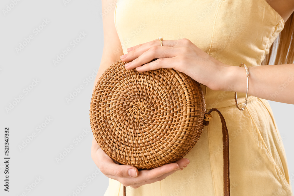 Woman with stylish jewelry holding rattan handbag on light background