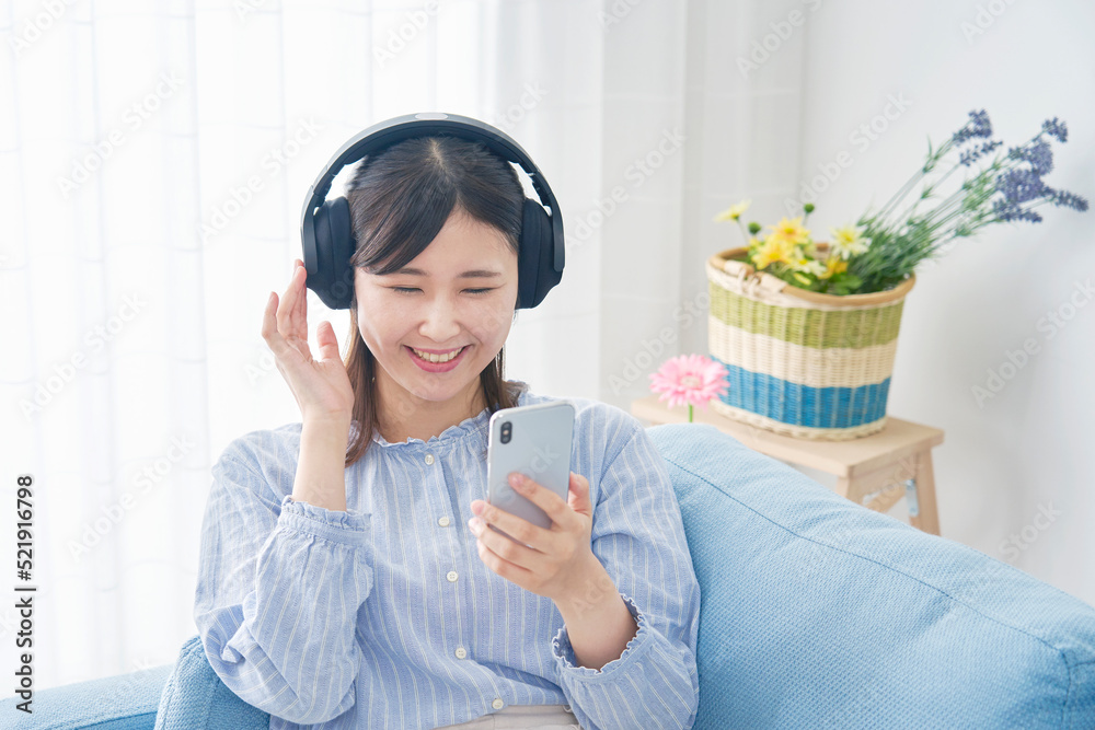 自宅でヘッドホンをしてスマホで音楽を聴く女性　