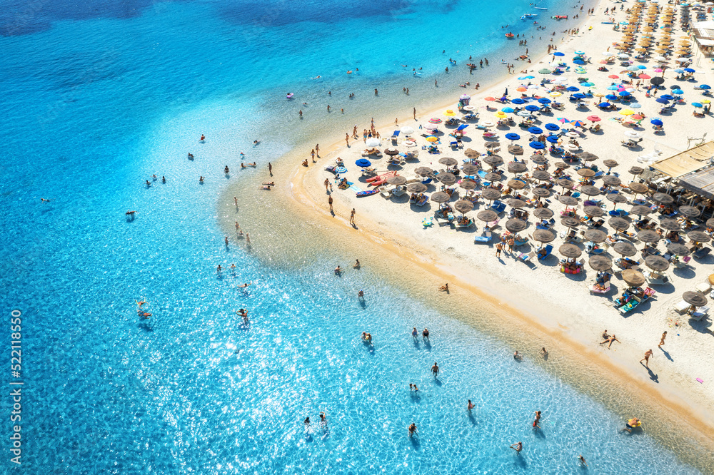 Aerial view of colorful umbrellas on sandy beach, people in blue sea at sunset in summer. Tuerredda 