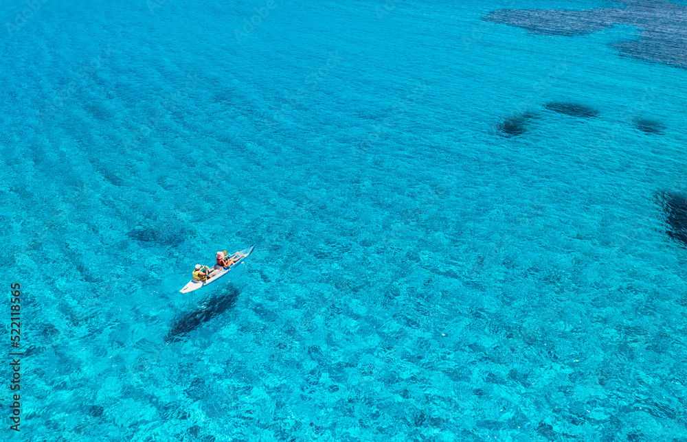 夏日日落时，人们在蓝色大海中的皮划艇鸟瞰图。漂浮在独木舟上的男女