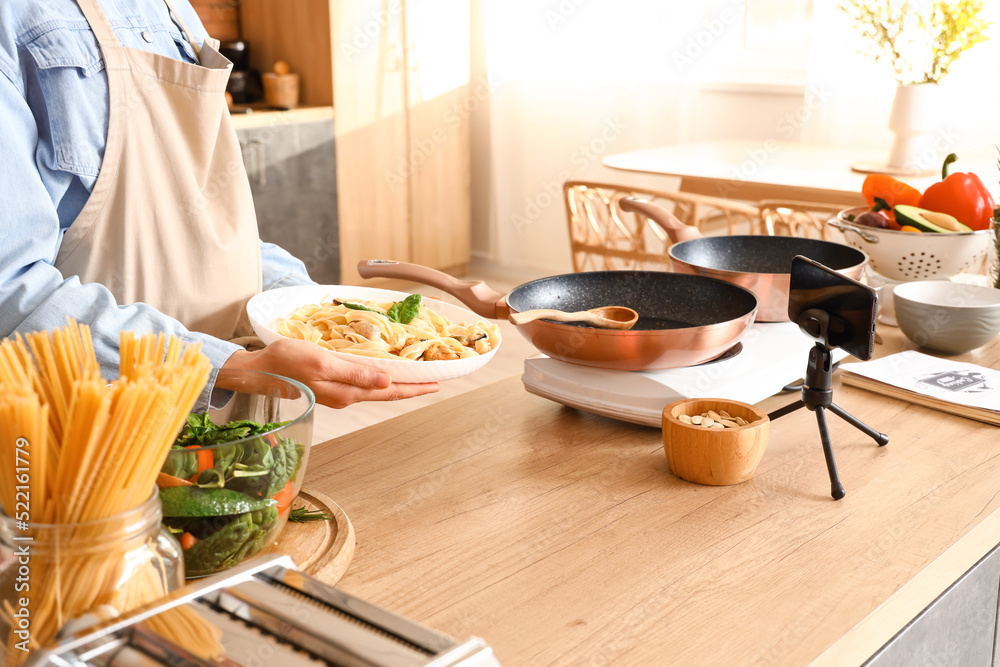 Young woman with tasty pasta recording video class in kitchen