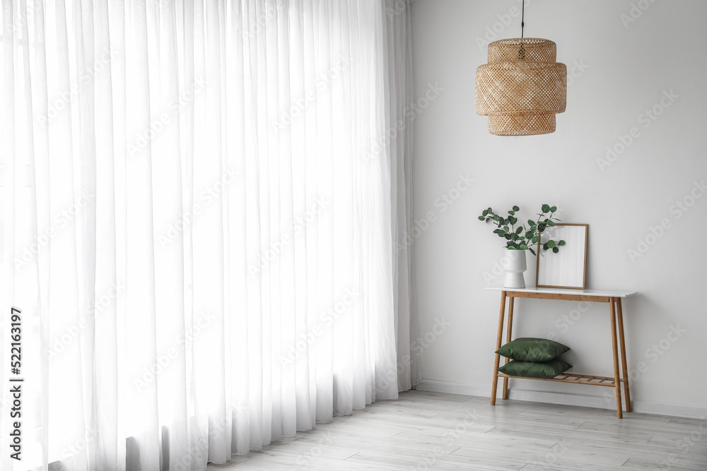 Shelving unit with vase, frame and pillows near light curtain in room