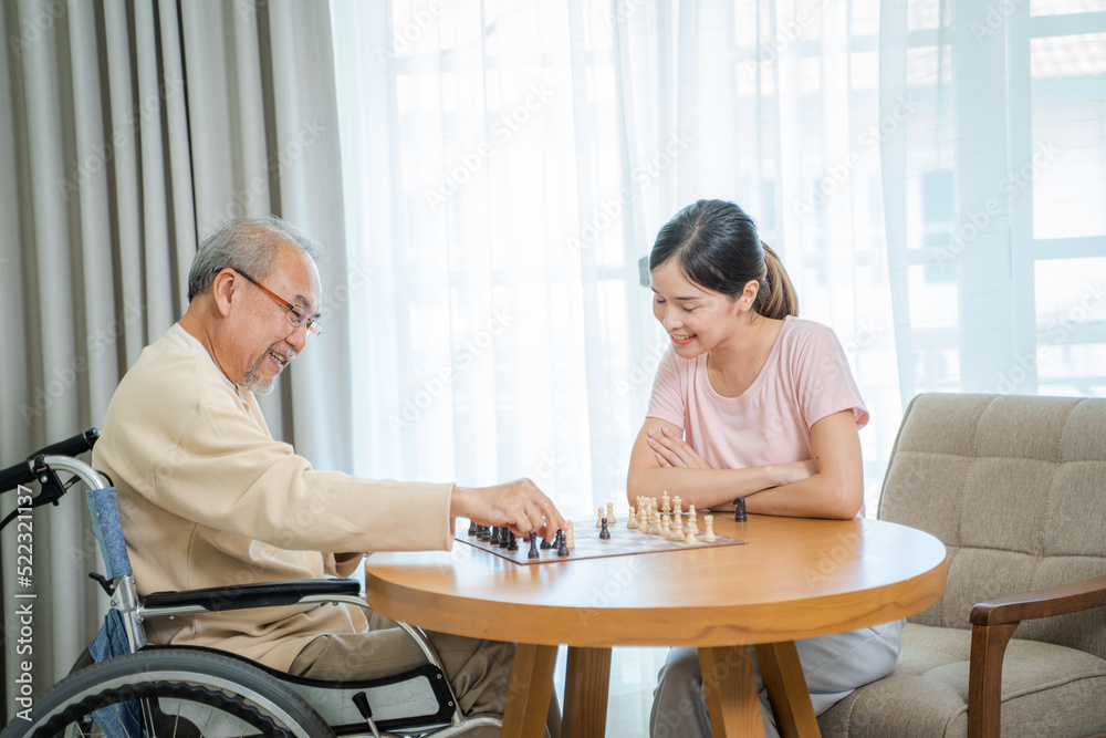 Senior man sitting on wheelchair playing chess together with daughter at nursing home.