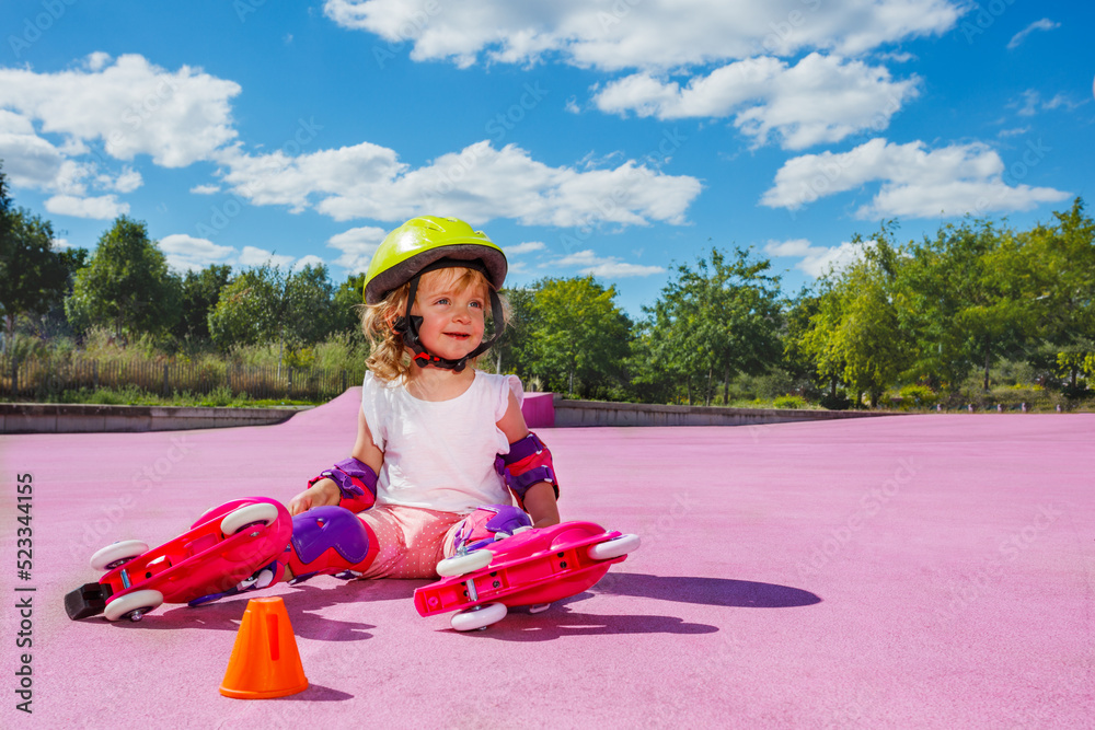 Cute small girl learn to skate rollers, sit in helmet and smile