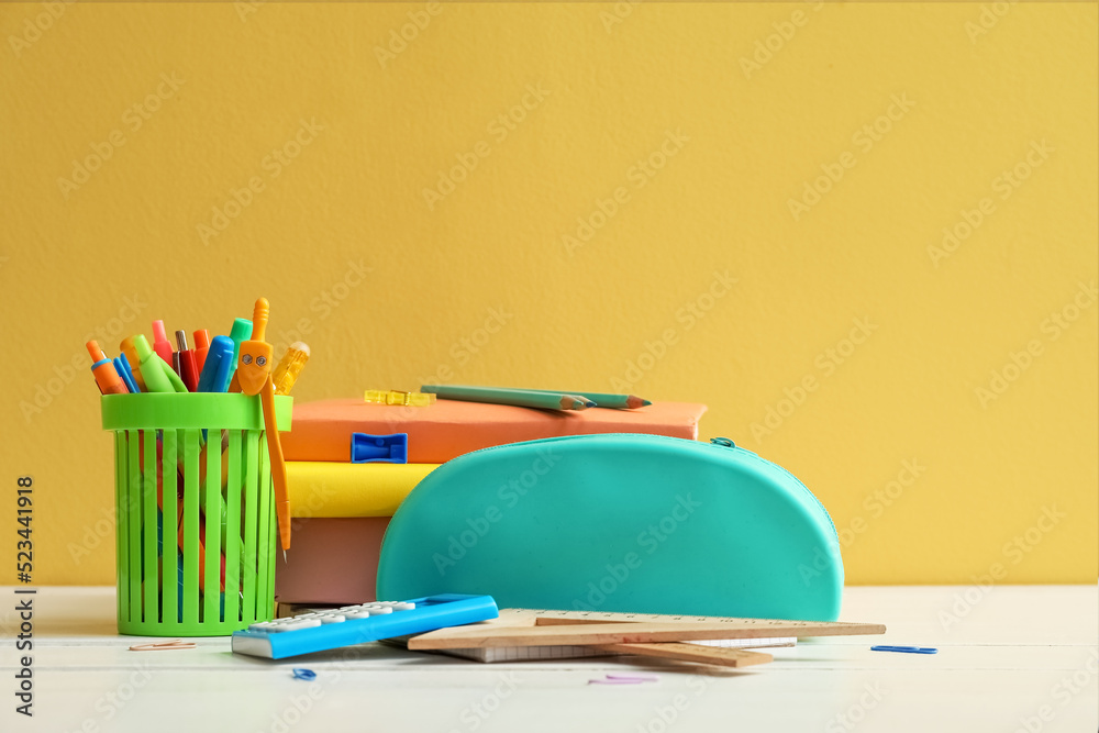 Pencil case with school stationery and pen cup on table against yellow background