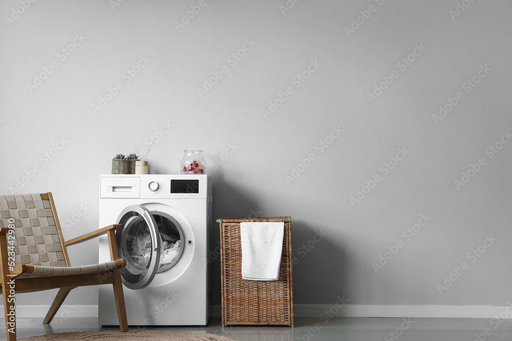 Interior of modern laundry room with washing machine, armchair and basket