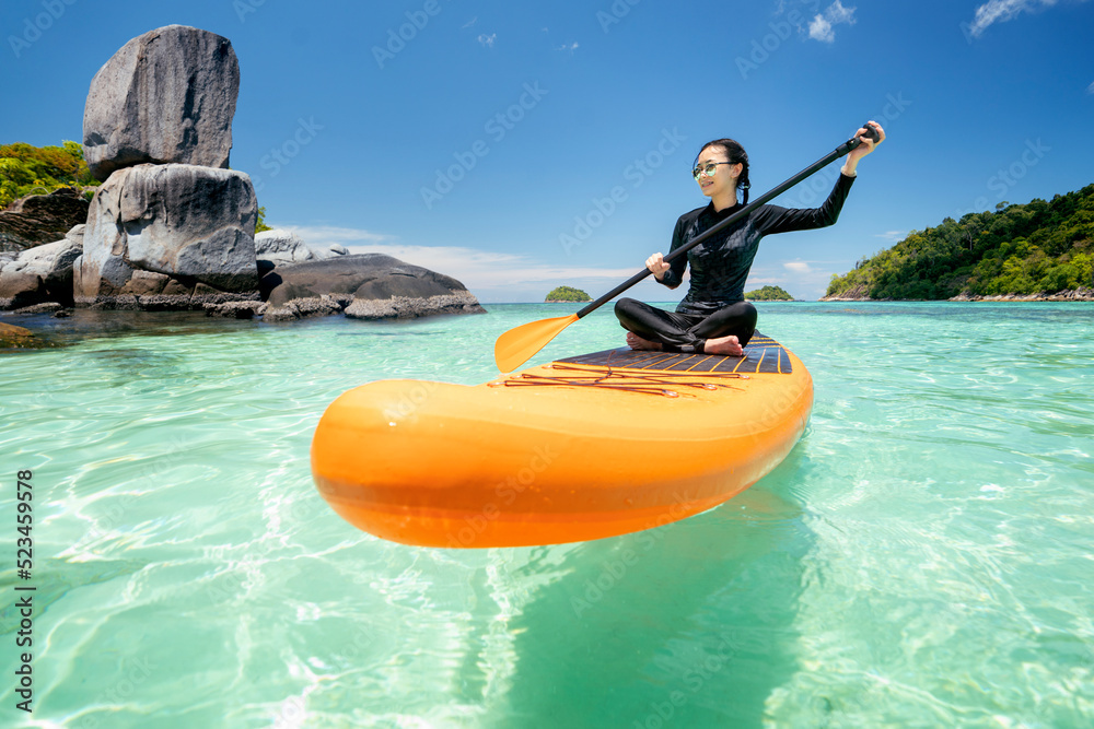 亚洲女人在海滩上用SUP BOARD放松