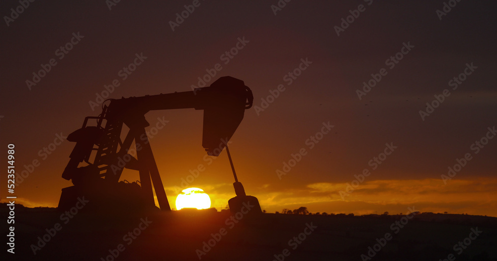 Image of oil pump working over sunset and landscape in background