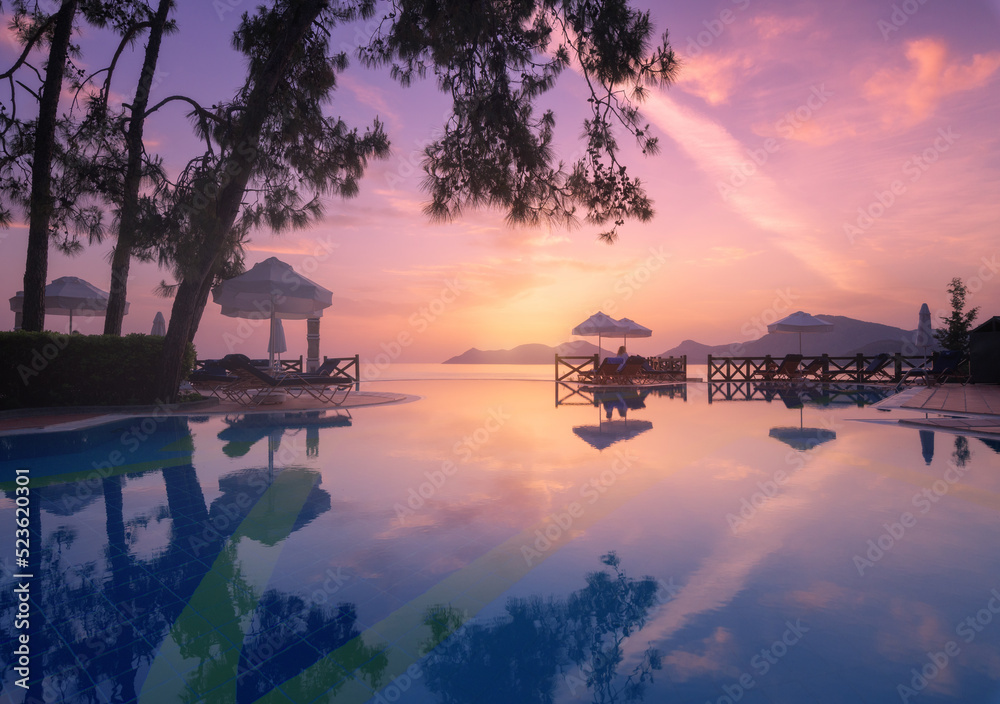 Beautiful reflection in swimming pool at colorful sunset. Purple sky reflected in water, palm trees,