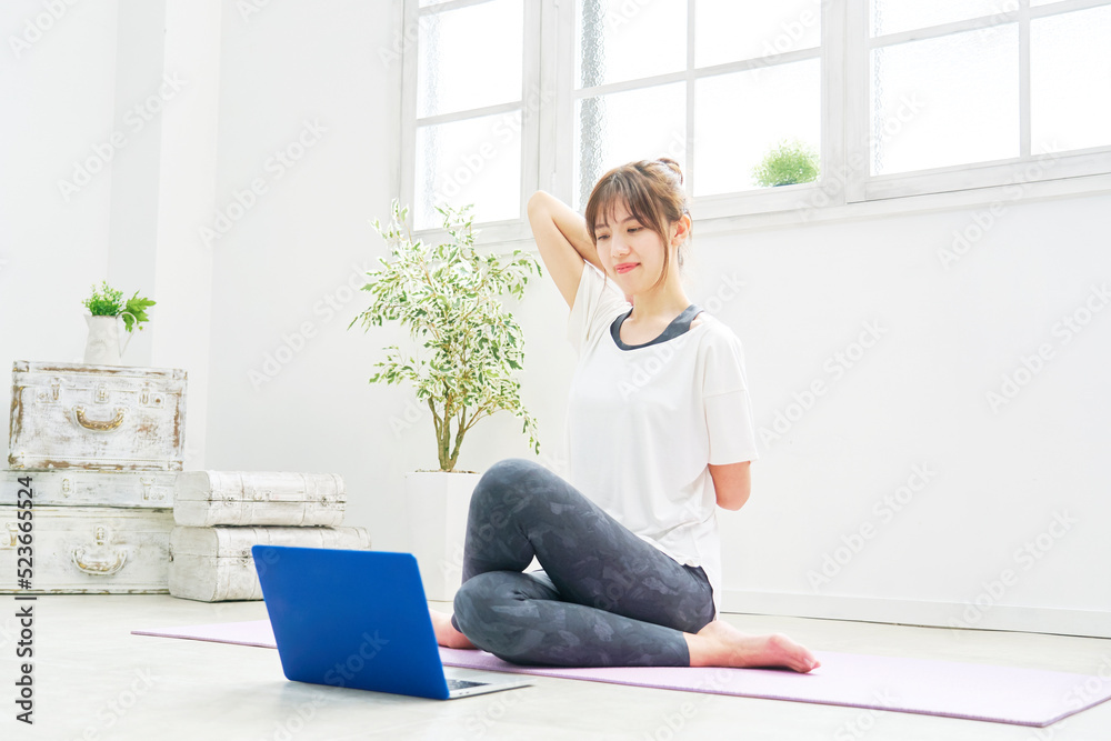 自宅でオンラインヨガで牛の顔のポーズをする女性