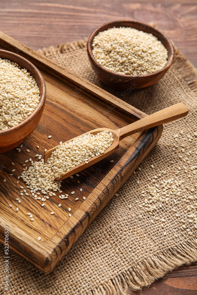 Board with scoop of sesame seeds on wooden table, closeup