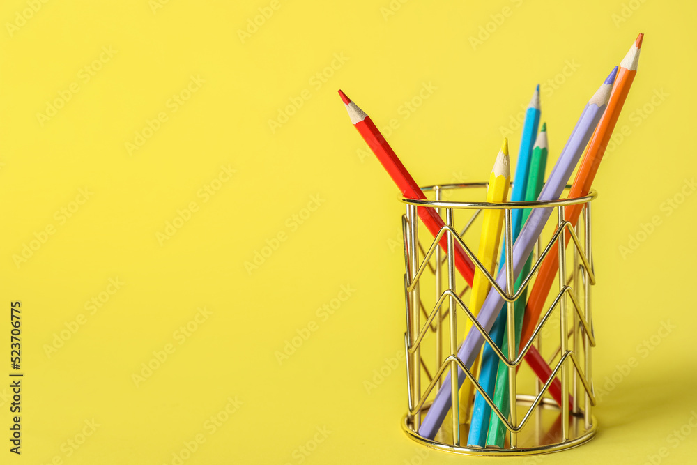 Golden cup with pencils on yellow background