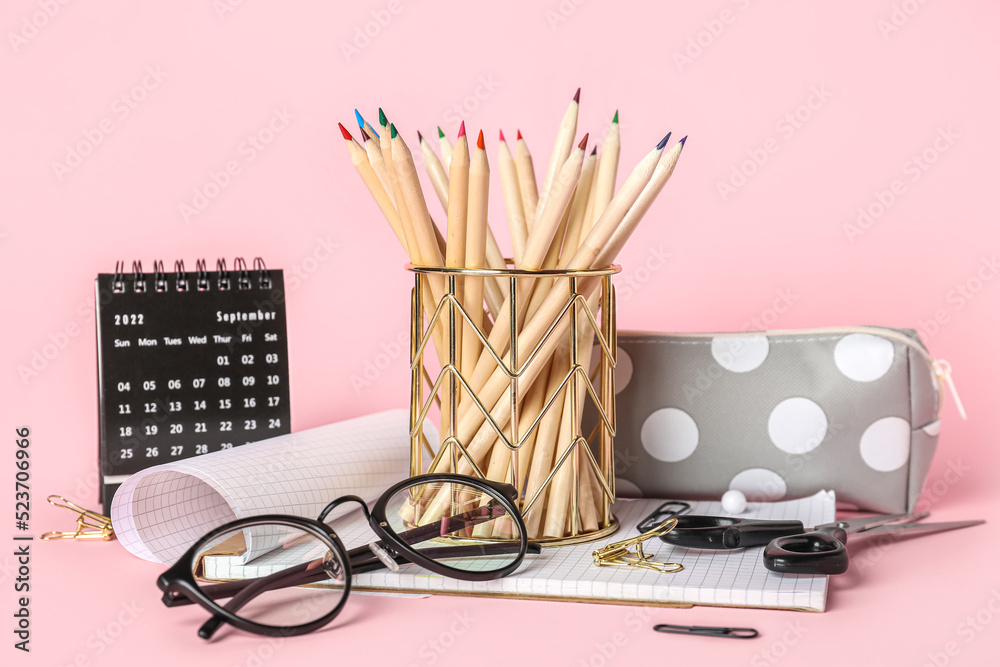 Cup with school stationery, eyeglasses and calendar on pink background