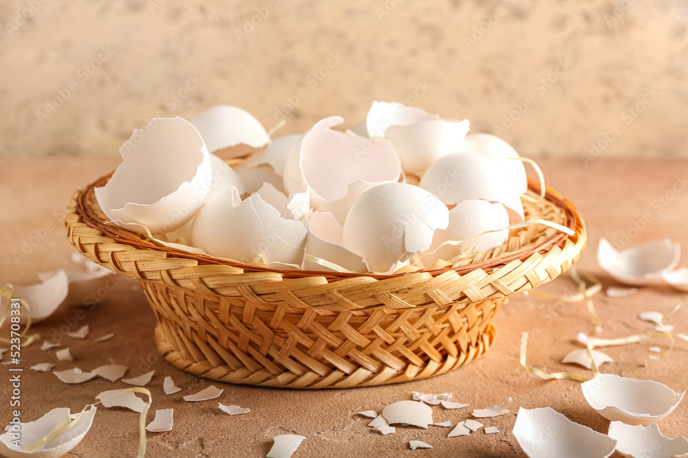 Basket with broken egg shells on beige background