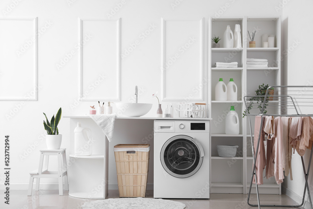 Interior of light laundry room with washing machine, sink and shelving units