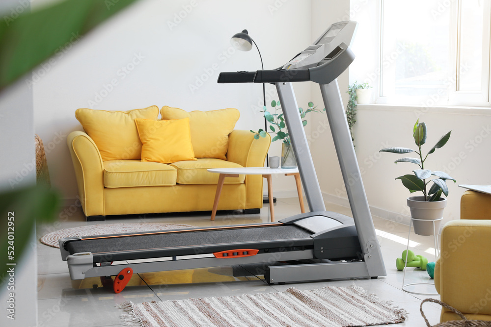 Interior of light living room with treadmill and yellow sofa