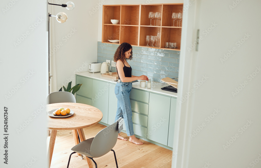 Young woman making tea, coffee or morning drink in a kitchen while relaxing at home. Female enjoying