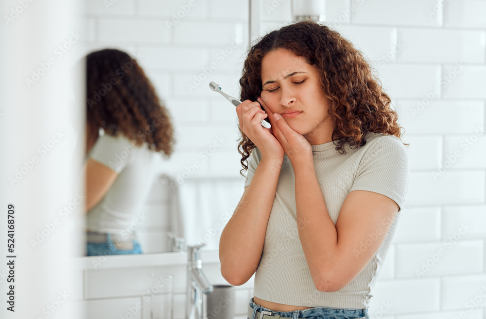 一个女人在家里的浴室里刷牙，引起牙痛、疼痛和牙齿敏感。年轻的fem