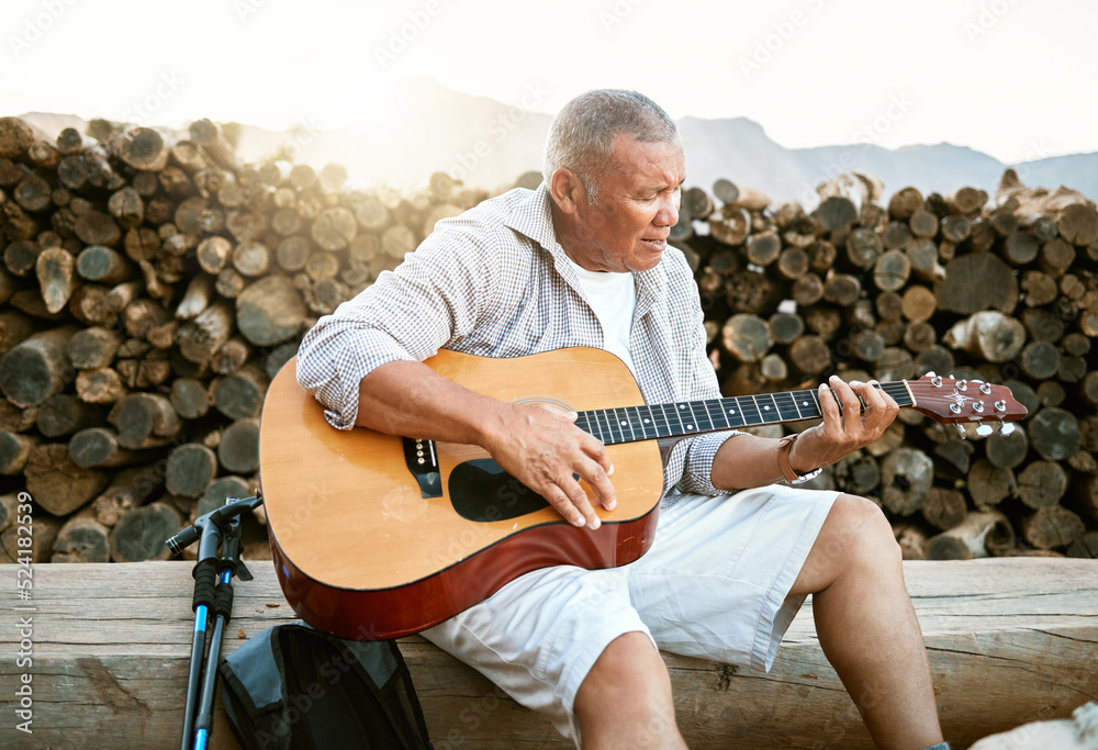 . Mature man, relaxing and playing the guitar while sitting outdoors and enjoying his hobby while ge