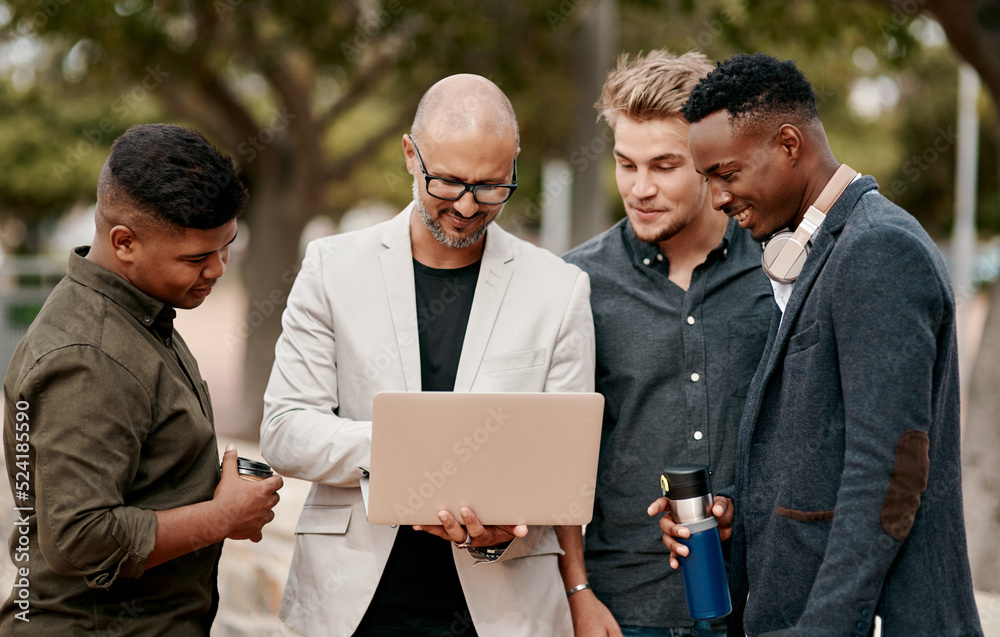 A team leader coaching his staff outdoors, standing and using a laptop. A group of male designers wo