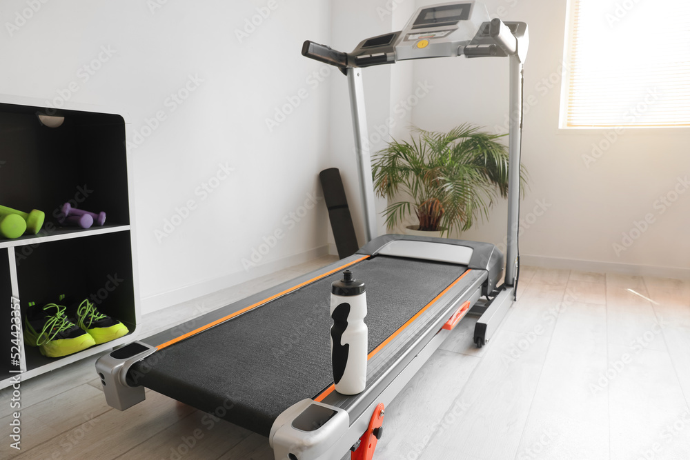 Modern treadmill with bottle of water in gym