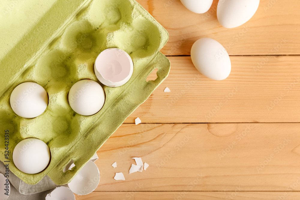 Cardboard holder with white chicken eggs and shells on wooden background