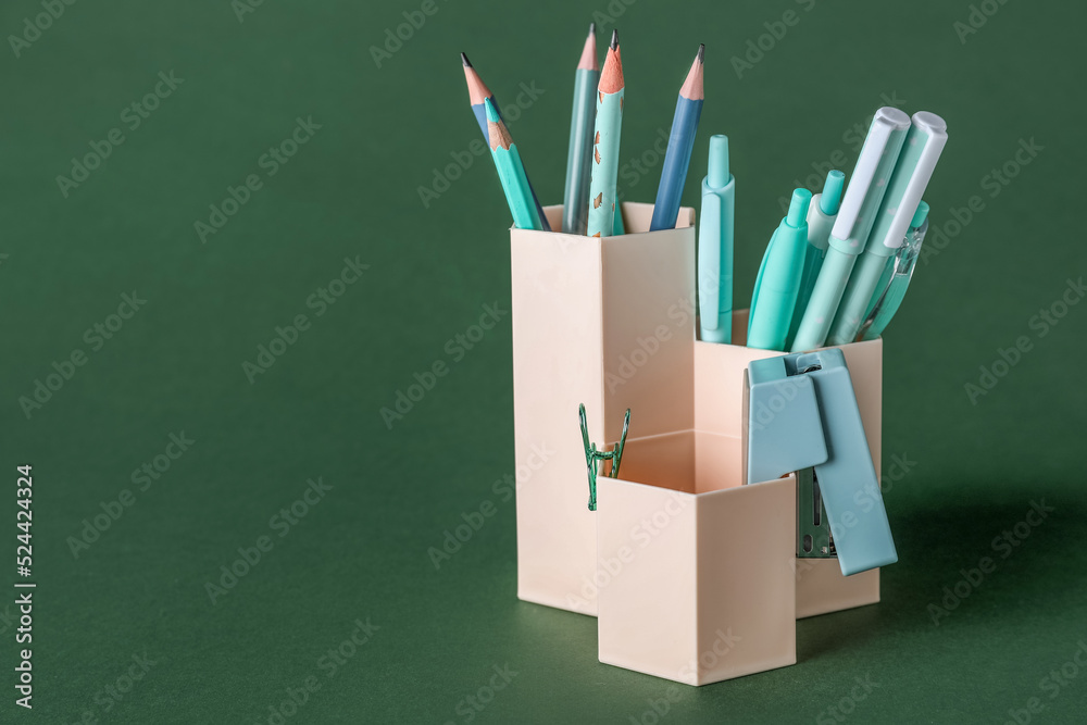 Cups with pens, pencils and stapler on green background