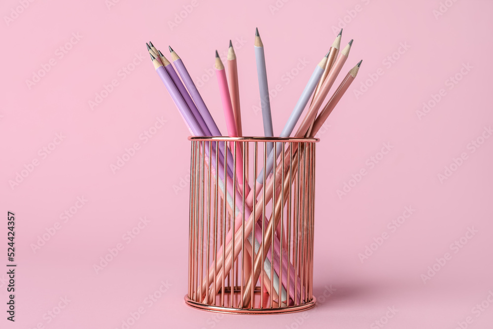 Metal cup with pencils on pink background