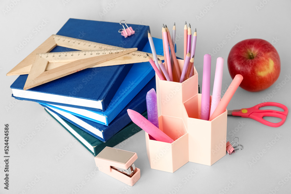 Cups with school stationery and apple on light background