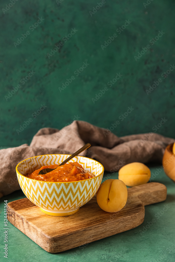 Wooden board with bowl of tasty apricot jam on color table