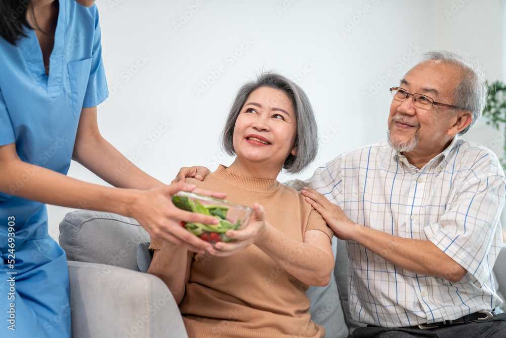 一位女护士为一对心满意足的老年夫妇端上一碗沙拉。医疗保健和医疗助理