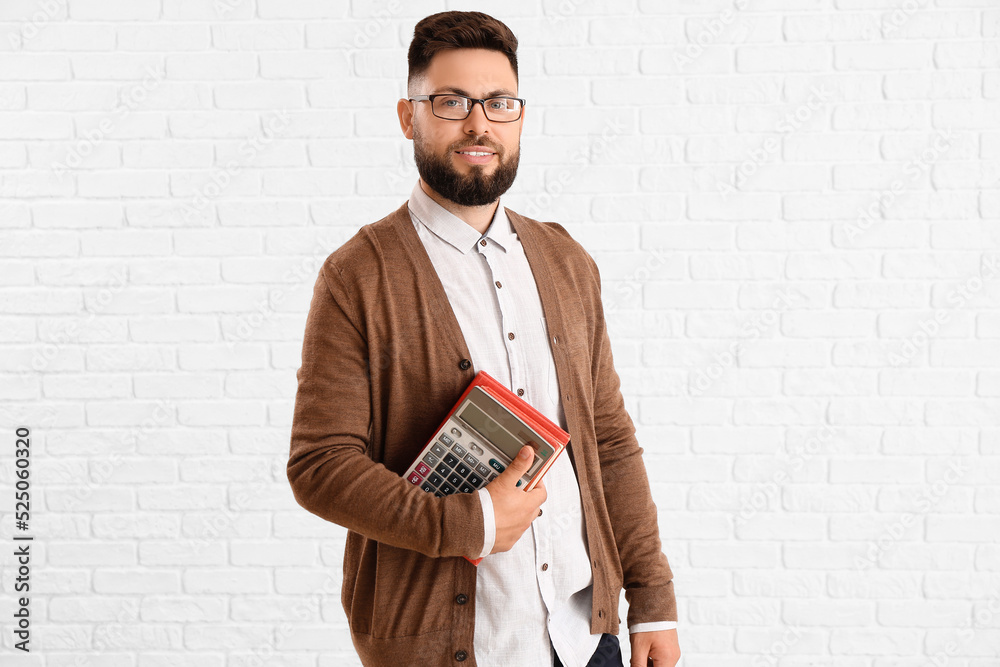 Handsome Math teacher with calculator and books on white brick background