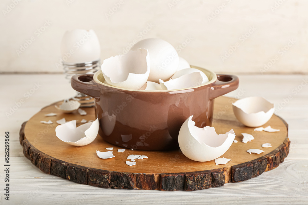 Board with broken egg shells in cooking pot on white wooden background