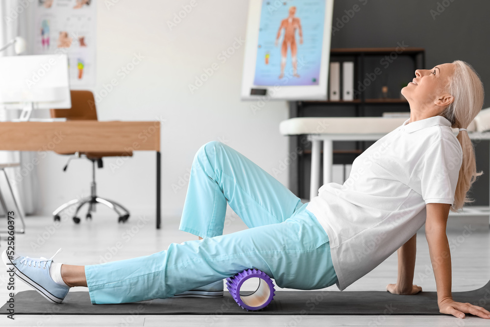 Mature physiotherapist training with foam roller in rehabilitation center