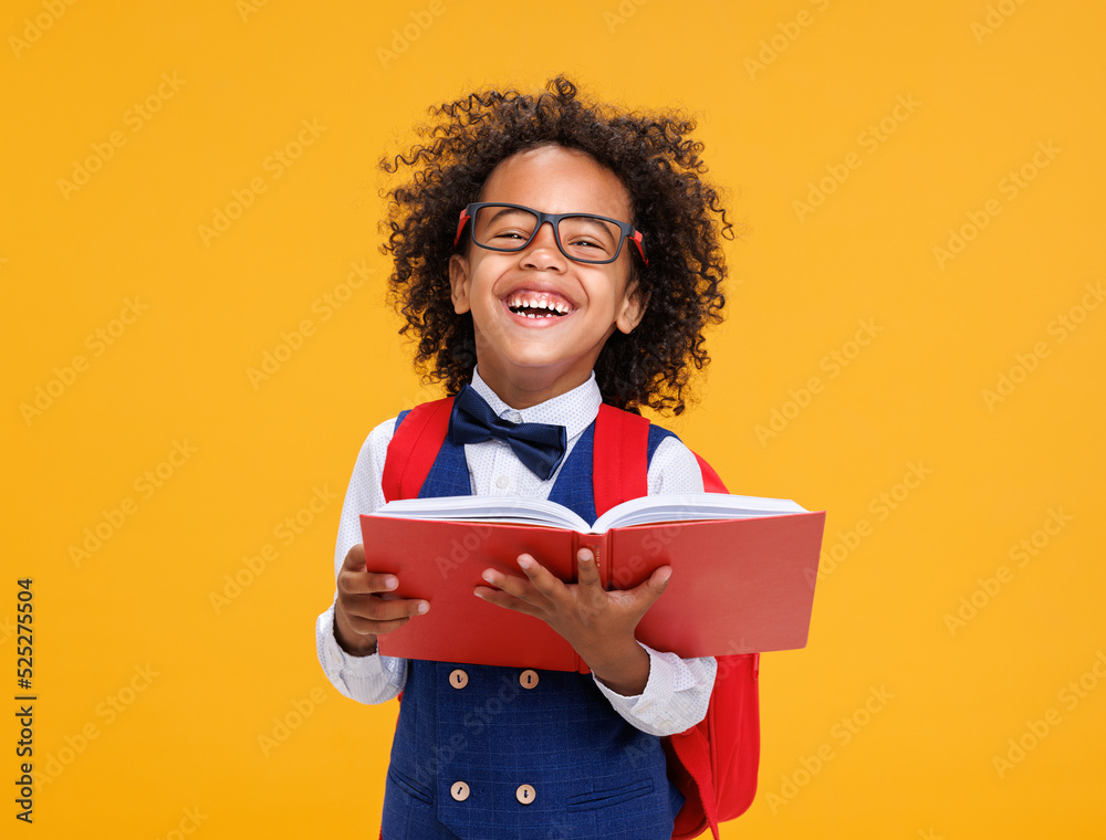 Happy ethnic schoolboy playing with book