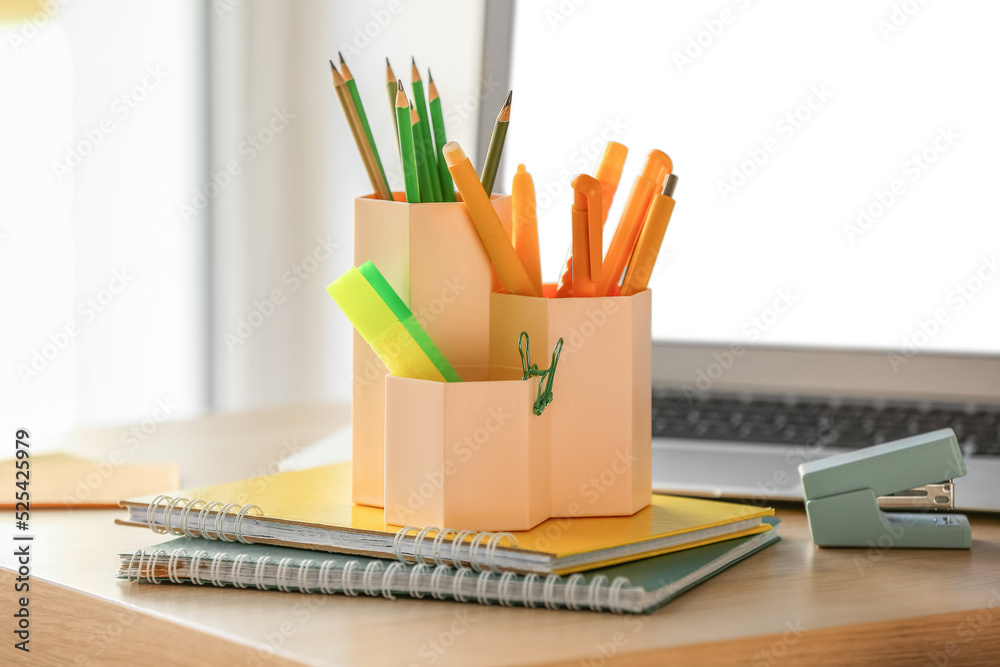 Cups with stationery and laptop on table in room, closeup