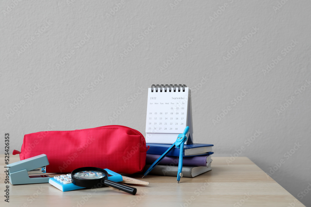 Red pencil case with school stationery and calendar on table against grey background