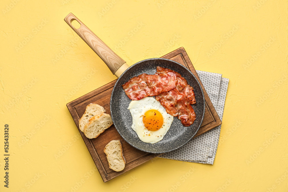 Wooden board with frying pan of tasty fried egg, bacon and bread on color background