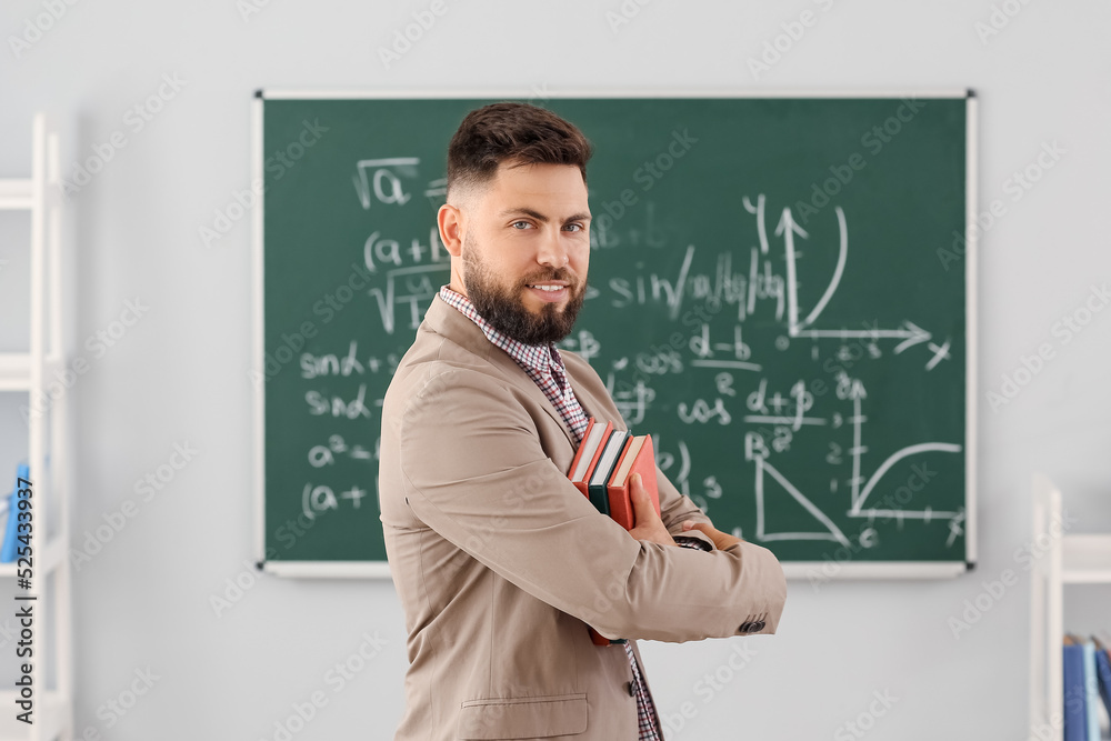 Handsome Math teacher with books in classroom