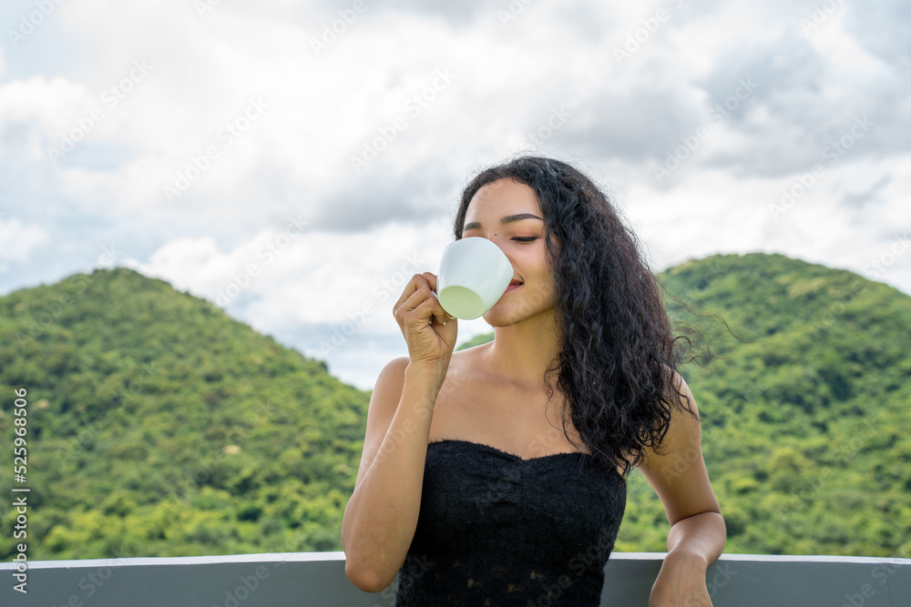 年轻的女人喝着一杯咖啡，脸上洋溢着幸福，站着，面带自信的微笑。