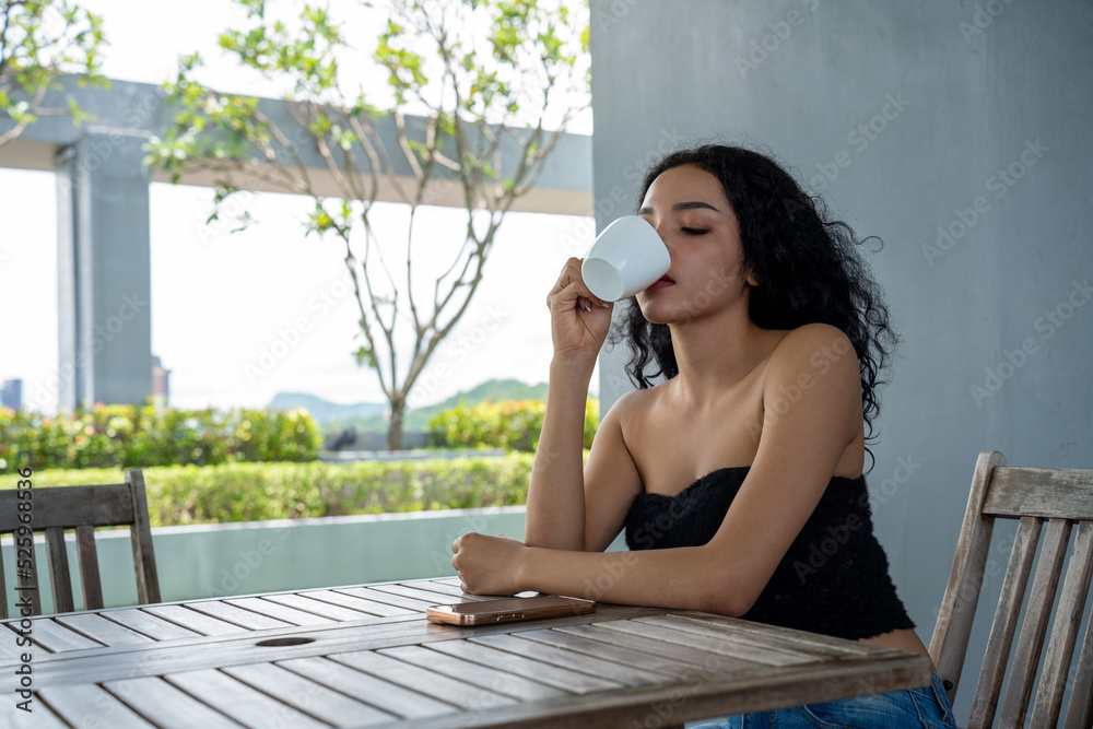 Young woman drinking a cup of coffee with a happy face standing and smiling with a confident smile. 