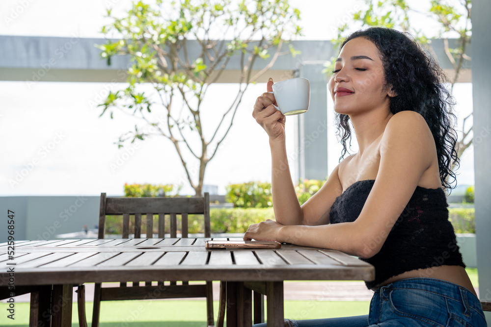 年轻的女人喝着一杯咖啡，脸上洋溢着幸福，站着，面带自信的微笑。