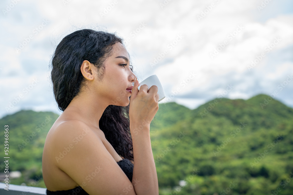 年轻的女人喝着一杯咖啡，脸上洋溢着幸福，站着，面带自信的微笑。