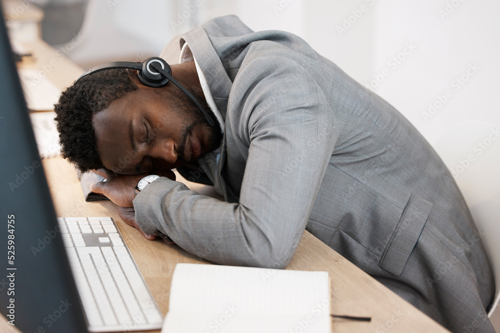 Tired CRM call center agent sleeping on computer desk at work office with headset on. Exhausted youn